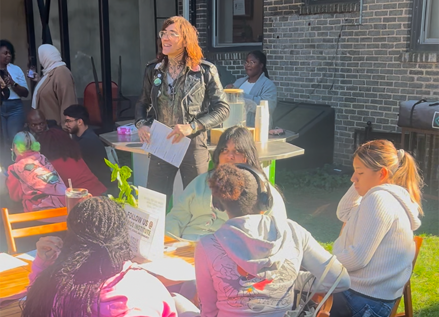 Teacher standing and facing students, sitting outside.