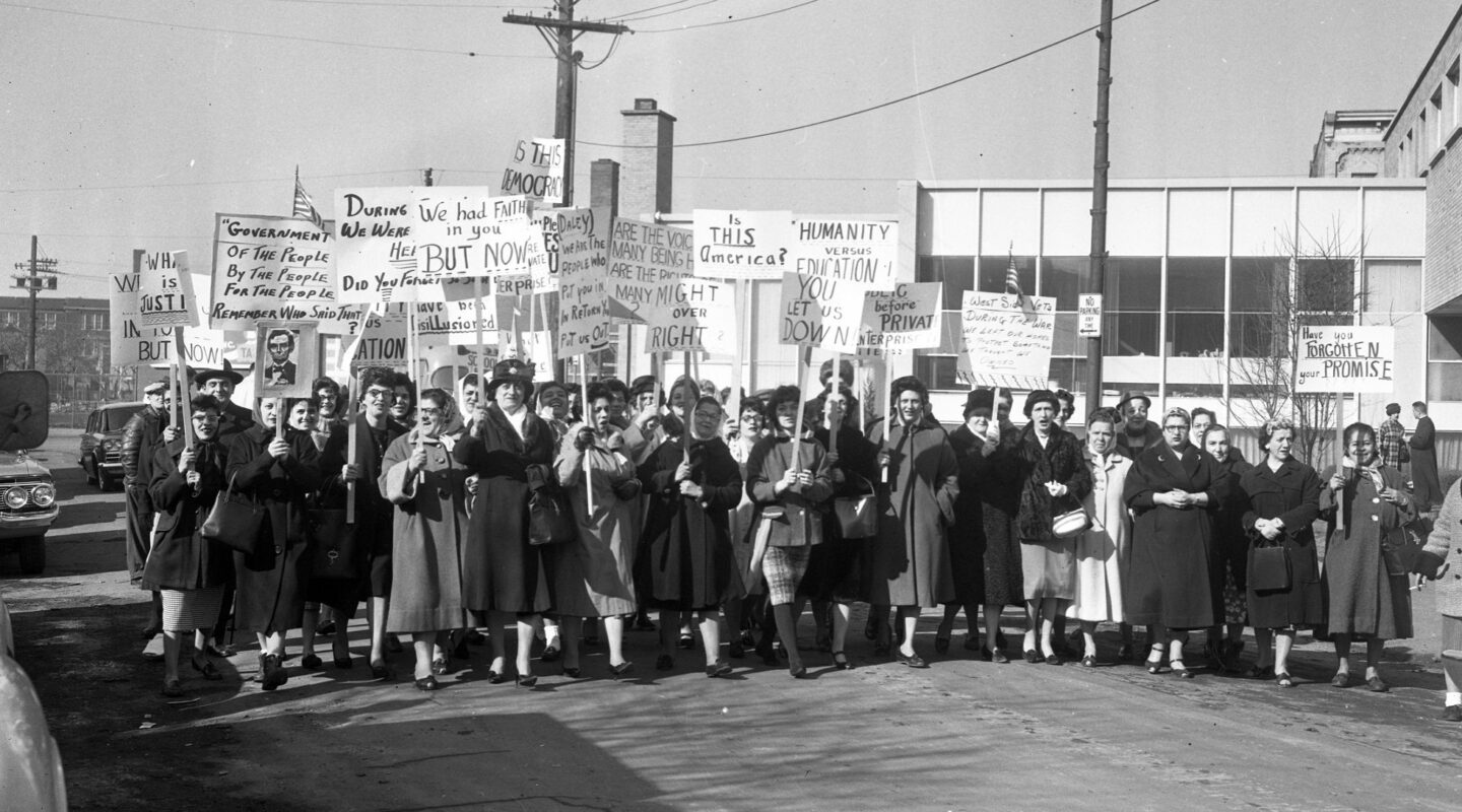 Black and White image of a protest from 1961. Protesters hold picket signs.