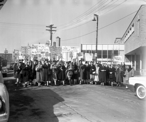 Black and White image of a protest from 1961. Protesters hold picket signs.