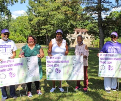 6 adults and one child stand in a park in front of picket signs that read 