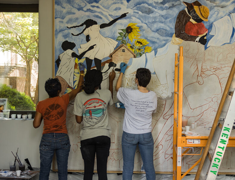 3 artists work on a mural in progress depicting the Jonesville community